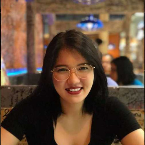 A smiling woman with medium-length dark hair, wearing a black top, in a warm, indoor environment.