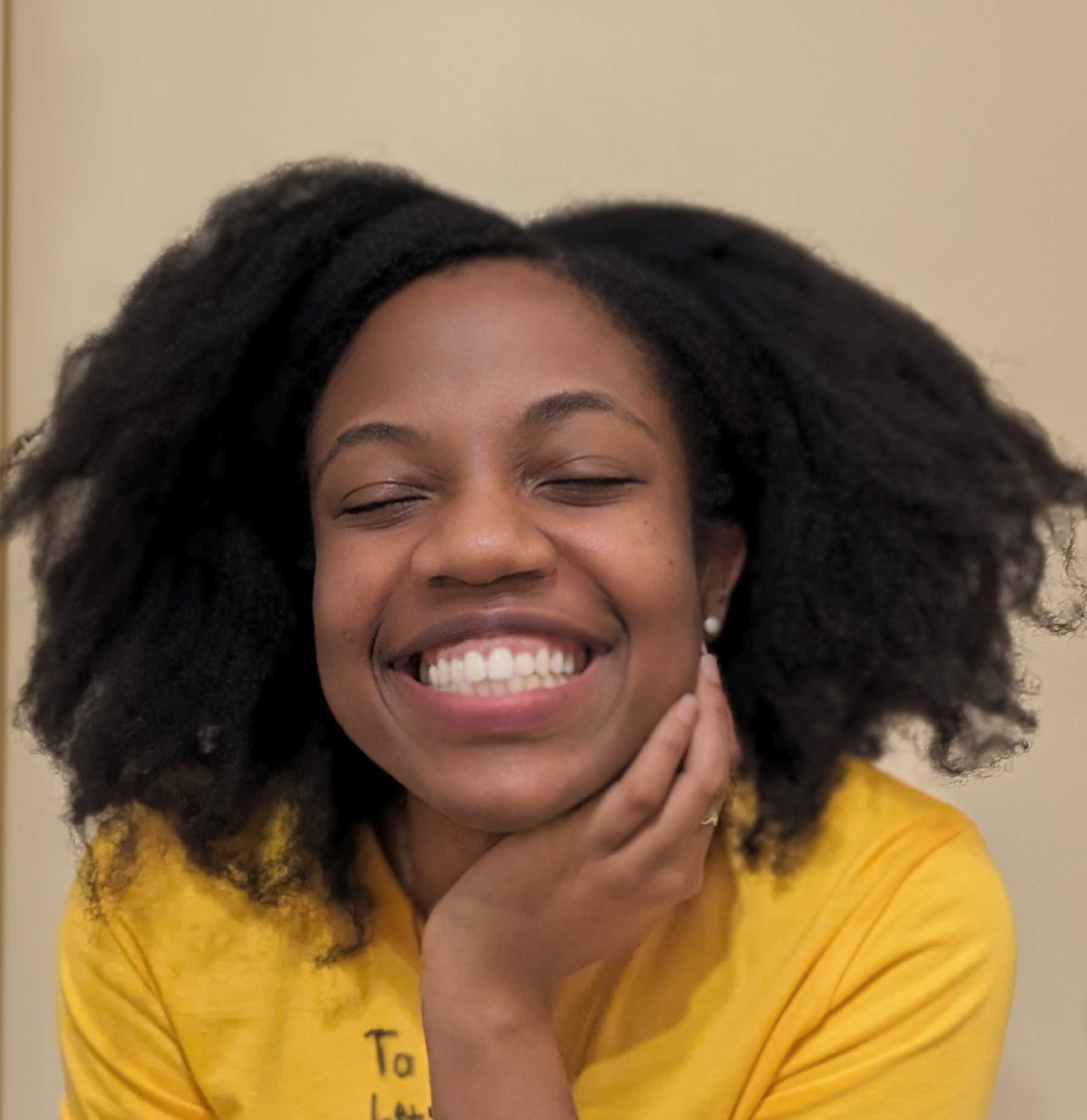 A smiling woman with dark curly hair, wearing a yellow shirt.